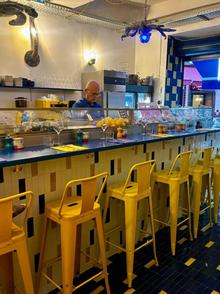 The counter of the Mer restaurant in Nice with an old-fashioned atmosphere, yellow stools, a counter with pale yellow, blue and pale pink mosaic.