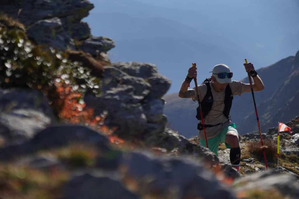 A runner with his poles climbing uphill in the mountains.
