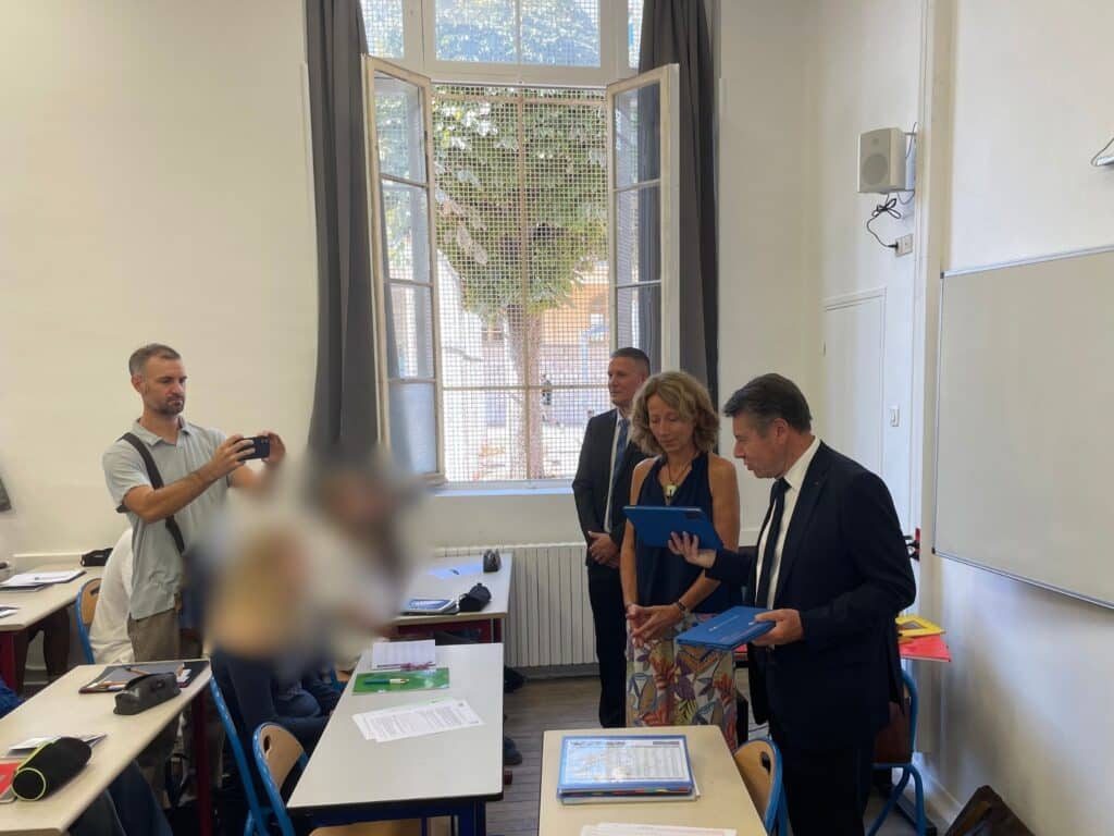 Christian Estrosi standing in a suit in a classroom holding tablets