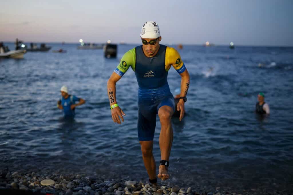 An athlete running on the pebbles of the Promenade des Anglais with his swimming cap and swimming goggles.