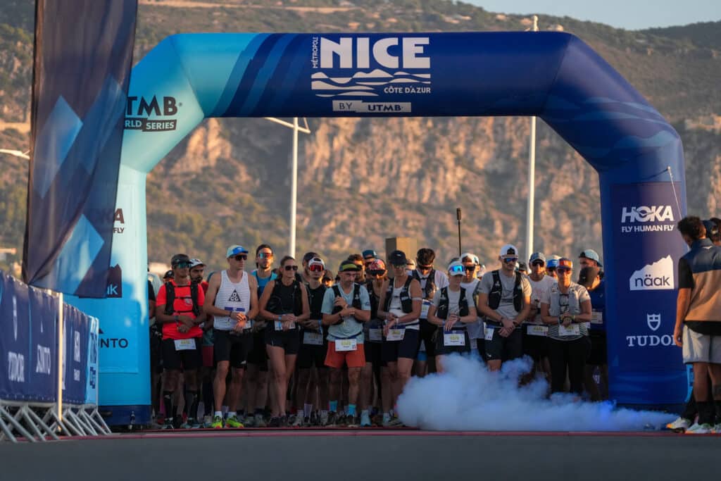 Athletes at the starting line of the 20k in front of a large blue arch.